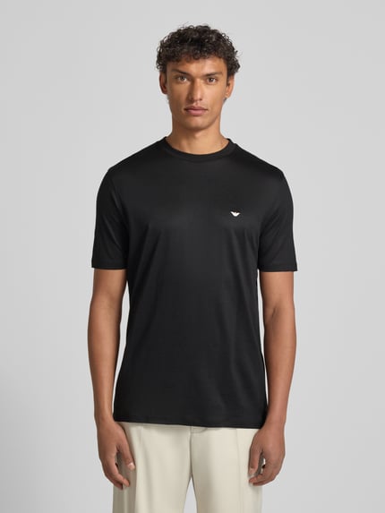 Männermodel trägt T-Shirt mit Label-Stitching von Emporio Armani, schwarz, Lyocell-Baumwoll-Mix, Regular Fit, gerippter Rundhalsausschnitt, Ganzkörperansicht von vorne.