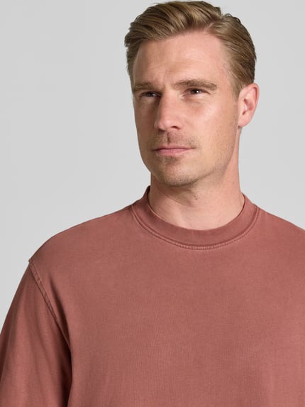 Männermodel trägt Boxy Fit T-Shirt aus reiner Baumwolle Modell 'CORY' von Selected Homme in matt-rostigem Rot, Nahaufnahme Oberkörper.