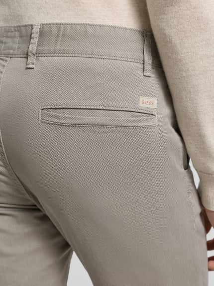 Männermodel draagt Slim Fit Chino aus Baumwoll-Mix Modell 'CHINO_SLIM' van BOSS Orange in beige met fijn structuurpatroon en label patch, detailopname heup.