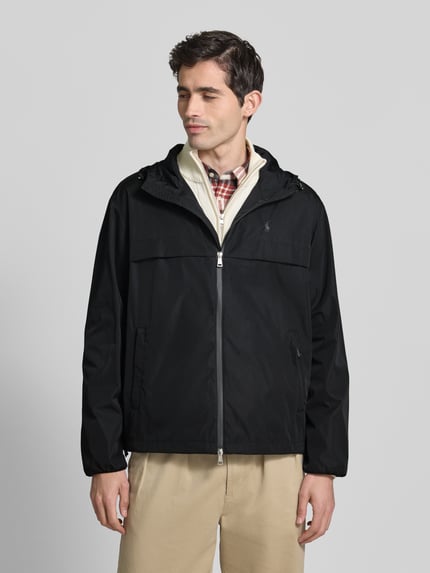 Männermodel trägt Regular Fit Regenjacke mit Logo-Stitching von Polo Ralph Lauren in Schwarz, Kapuze mit Tunnelzug, Zweiwege-Reißverschluss, seitliche Eingrifftaschen, Optik: Unifarben, Ganzkörperansicht von vorne.
