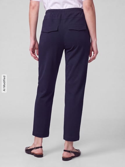 Frauenmodel trägt Barrel Leg Hose mit angedeuteten Taschen Modell 'Rachell' von Stehmann, einfarbig dunkelblau, Sweat-Material, Mid Waist, elastischer Bund, seitliche Eingrifftaschen, Ganzkörperansicht Rückansicht, KI-modifiziertes Bild.