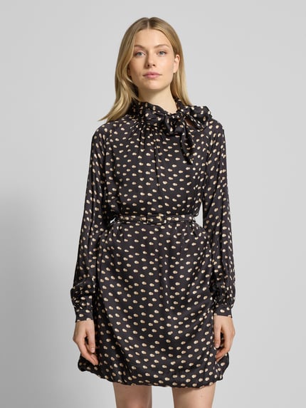 Frauenmodel trägt Cocktailkleid mit Stehkragen von Rinascimento, schwarze Viskose mit beigefarbenem Muster, taillierter Schnitt, Schleifen-Detail, Taillengürtel mit Dornschließe, Rückenlänge 87 cm, Brustweite 61 cm, Ärmellänge 62 cm, Ganzkörperansicht von vorne.