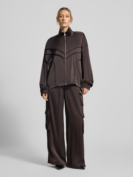 Frauenmodel trägt Relaxed Fit Jacke mit Stehkragen Modell 'Darzi' von Gestuz in Dunkelbraun, glatte Textur, Ganzkörperansicht von vorne. Rückenlänge 62 cm, Schulterbreite 44 cm, Brustweite 65 cm, Ärmellänge 56 cm, elastischer Material-Mix.