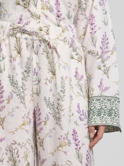 Vrouwenmodel draagt Wide Leg Leinenhose mit Lavendelprint van Christian Berg Woman, zuiver linnen, wide fit, bloemenmotief, elastische band, detailopname.