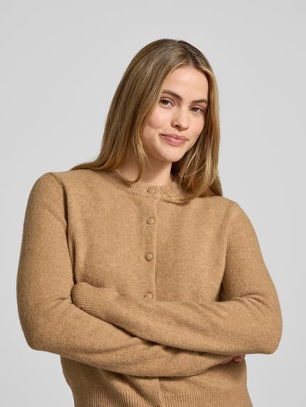 Frauenmodel trägt Cardigan mit Rundhalsausschnitt Modell 'SEEDSUN' von Mango, beige, weiche Textur, Knopfleiste, Regular Fit, Nahaufnahme Oberkörper.