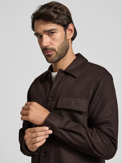 Męski model nosi Regular Fit Hemdjacke mit Kentkragen und Brusttaschen von Profuomo, brązowy materiał z domieszką wełny, krój regular fit, zapięcie na guziki, kieszenie na piersi, długość pleców w rozmiarze M: 76 cm, zbliżenie na górną część ciała