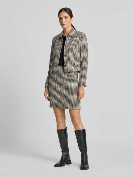 Frauenmodel trägt Minirock mit angedeuteten Pattentaschen und Zierknopf von Christian Berg Woman Selection, Material-Mix mit Viskose-Anteil, Straight Fit, schwarz-weißes Karomuster, Vorder- und Rückseitiger Knopf- und Reißverschluss, mittlere Bundweite, mittlere Länge, Ganzkörperansicht von vorne.