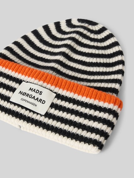 Produktfoto, Beanie aus reiner Wolle Modell 'Anju' von MADS NØRGAARD, gestrickte Optik mit schwarzen und weißen Streifen, breiter oranger Umschlag, Label-Patch, Kontraststreifen.