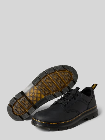 Produktfoto, schwarze Schuhe aus echtem Leder Modell 'Reeder' von Dr. Martens mit gelber Naht, profilierte Sohle, grauer Hintergrund.