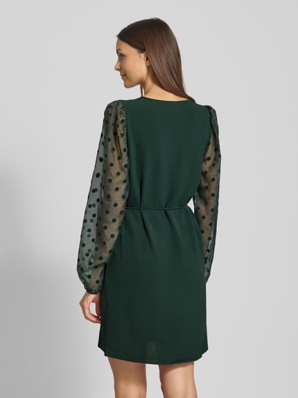 Frauenmodel trägt fließendes Cocktailkleid mit semitransparenten Ballonärmeln Modell 'ALVA' von Vero Moda, Optik: Unifarben, Passform: fließend, Mini-Länge, V-Ausschnitt, Ärmelabschluss: elastisch, Materialverarbeitung: Crinkle, Ganzkörperansicht Rückansicht.