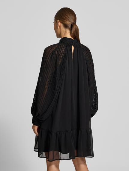 Frauenmodel trägt Minikleid mit Stehkragen Modell 'OLERA' von YAS, schwarzer fließender Stoff, Rückenansicht, Ganzkörperansicht Rückansicht. A-Linie, lange Ärmel, luftige Textur, Rückenlänge 85 cm, Brustweite 50 cm, Ärmellänge 60 cm.