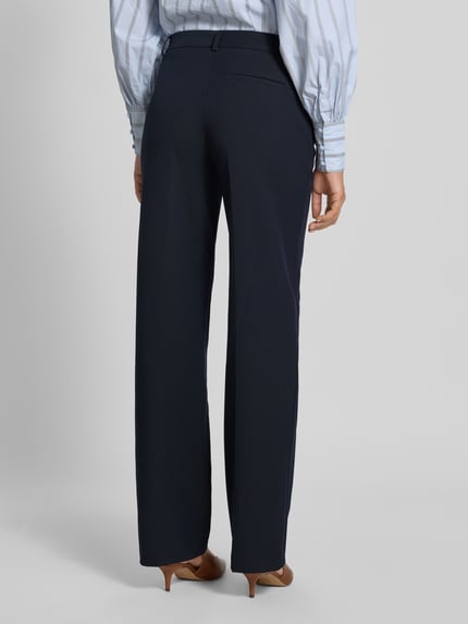 Vrouwenmodel draagt Stoffhose mit weitem Bein und Bügelfalten van Christian Berg Woman Selection in donkerblauw, gladde stof, paspelzak achter, materiaal-mix met viscose-aandeel, wijde pijp, full body achteraanzicht.