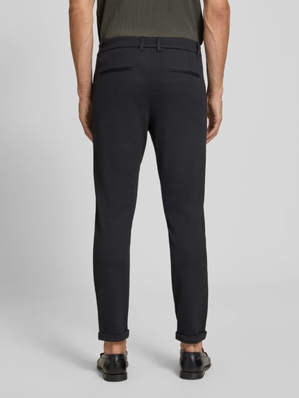 Męski model nosi Slim Fit Hose mit Viskose-Anteil in verkürzter Passform von Lindbergh, czarne, mieszanka wiskozy, kieszenie z tyłu, krój slim fit, szerokość w rozmiarze M: 42 cm, długość wewnętrzna nogawki: 72 cm, materiał elastyczny, widok całej sylwetki od tyłu.