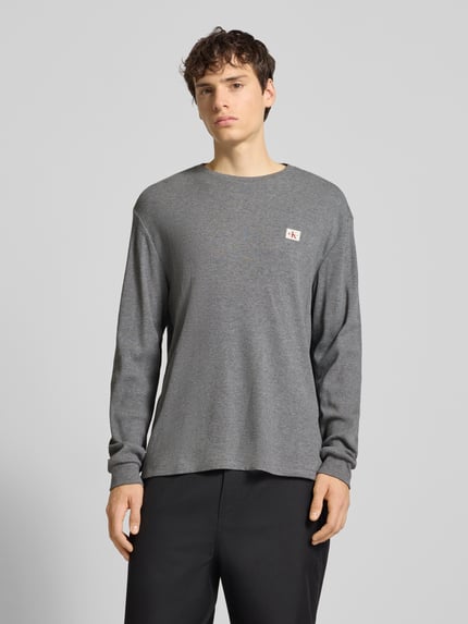 Männermodel trägt graues Slim Fit Longsleeve mit Logo-Patch Modell 'Waffle' von Calvin Klein Jeans, Baumwoll-Mix, Piqué, Ganzkörperansicht von vorne.