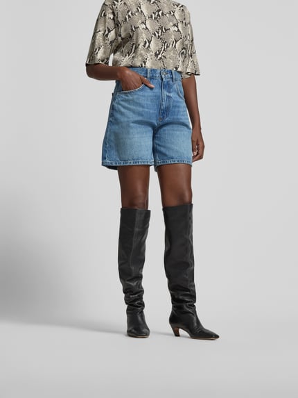 Frauenmodel trägt Jeansshorts aus reiner Baumwolle von Anine Bing in A-Linie mit 5-Pocket-Design, Knopf-Reißverschluss und Kontrast-Nähten, mittleres Blau, glatte Textur, Ganzkörperansicht von vorne.