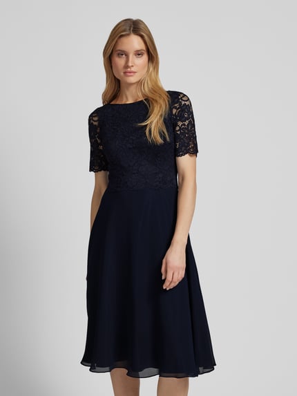 Frauenmodel trägt Cocktailkleid mit Spitzenbesatz von Vera Mont, unifarbenes Design, Material-Mix mit Stretch-Anteil, Ganzkörperansicht von vorne.