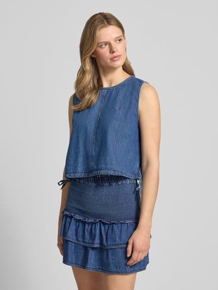 Frauenmodel trägt Relaxed Fit Denim Blusentop aus reiner Baumwolle von Tommy Jeans in Denim-Optik mit Rundhals-Ausschnitt, Cropped-Länge und Tunnelzug am Rumpfabschluss, Ganzkörperansicht von vorne.