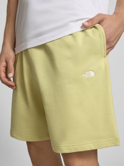 Männermodel trägt Sweatshorts mit Logo-Stitching von The North Face in Gelb, Reine Baumwolle, Relaxed-Fit, Nahaufnahme Oberschenkel.