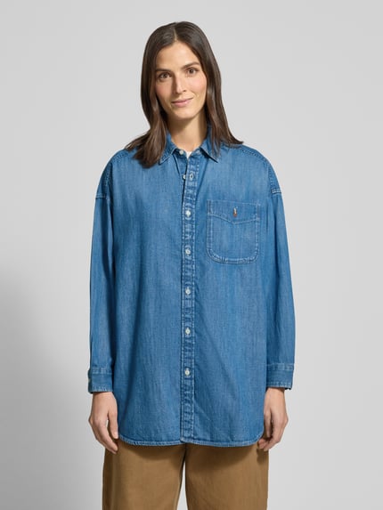 Frauenmodel trägt Oversized Hemdbluse in Denim-Optik von Polo Ralph Lauren aus reiner Baumwolle mit Hemdblusenkragen, Knopfleiste, Brusttasche und Label-Stitching, Rückenlänge 85 cm, Ärmellänge 50 cm, Ganzkörperansicht von vorne.