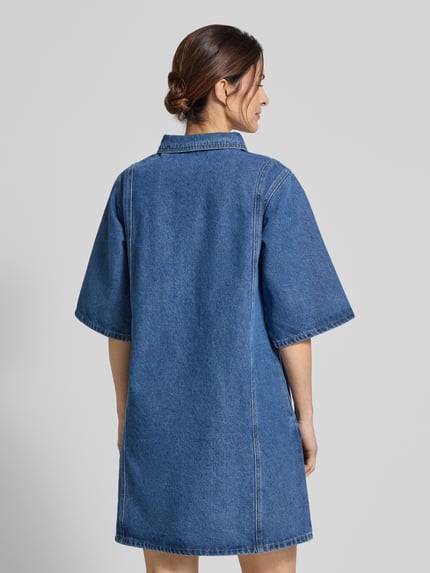 Frauenmodel trägt Jeanskleid mit Brusttaschen Modell 'Mola' von LOLLYS LAUNDRY, Baumwoll-Viskose-Mix, Gerader-Schnitt, Minikleid, Ganzkörperansicht Rückansicht.