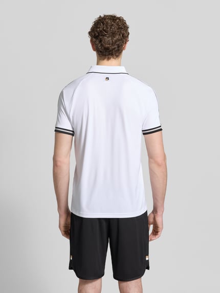 Mężczyzna-model nosi Regular Fit Poloshirts mit Kontrastdetails von BOSS Green, kolor biały z czarnymi akcentami, krój regular fit, kołnierzyk polo, zapięcie na dwa guziki, optyka two tone, całopostaciowy widok z tyłu.