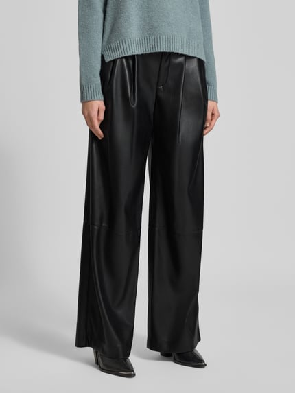 Frauenmodel trägt Relaxed Fit Weite Hose mit Bundfalten Modell 'TADESA' von BOSS in glänzender Optik aus Kunstleder, Nahaufnahme Unterkörper.
