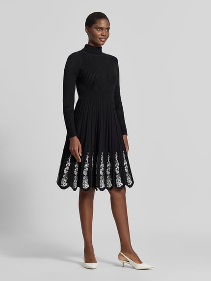 Frauenmodel trägt Knielanges Strickkleid aus Viskose-Mix von Apricot mit Stehkragen, floralen Stickereien, A-Linien-Rock, Ganzkörperansicht von vorne.