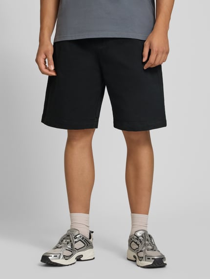 Männermodel trägt Shorts aus Baumwoll-Mix Modell 'Floyde' von Carhartt Work In Progress in Schwarz, Relaxed Fit, Ganzkörperansicht von vorne.
