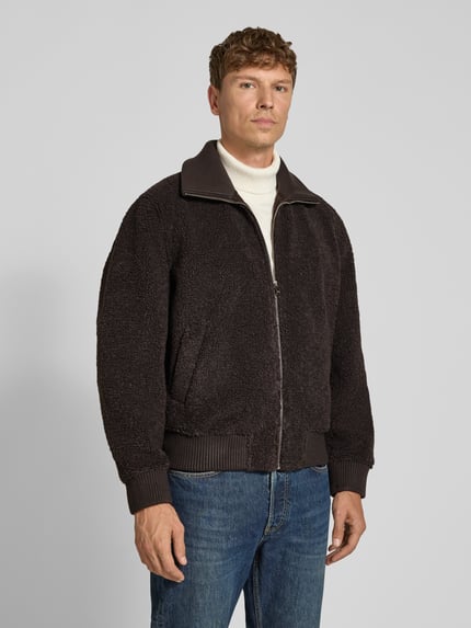 Männermodel trägt Jacke mit Stehkragen und Reißverschluss Modell 'GRALON' von DRYKORN aus braunem Teddyfell, Regular Fit, Ganzkörperansicht von vorne.