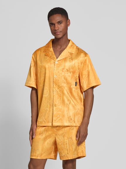 Mannmodel draagt Relaxed Fit vrijetijdsoverhemd met reverskraag model 'Resort' van COLUCCI in glanzend oranjetint met paisleypatroon, elastische materiaalmix, borstzak, logopatch, knoopsluiting, ruglengte maat M 70 cm, schouderbreedte 56 cm, mouwlengte 26 cm, geheel van voren.