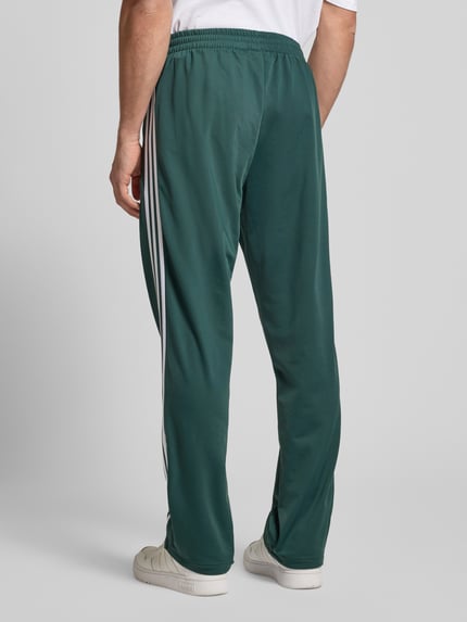Männermodel draagt Sweatpants met elastische tailleband van adidas Originals in los groen met witte strepen, productdetails zichtbaar, Ganzkörperansicht Rückansicht.