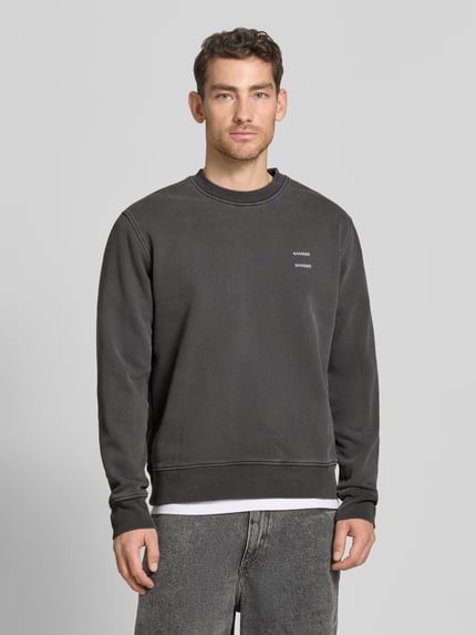 Męski model nosi Sweatshirt mit Logo-Print Modell 'JOEL' od Samsøe Samsøe, bawełniany miks, krój relaxed fit, melanż szarości, nadruk logo, prążkowany okrągły dekolt, długość tyłu w rozmiarze M 67 cm, długość rękawa w rozmiarze M 66 cm, widok całej sylwetki z przodu