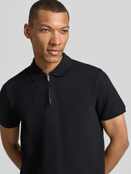 Männermodel trägt Regular Fit Poloshirt mit Strukturmuster von MCNEAL, Kurzarm, Reißverschluss, schwarze Farbe, Nahaufnahme Oberkörper.