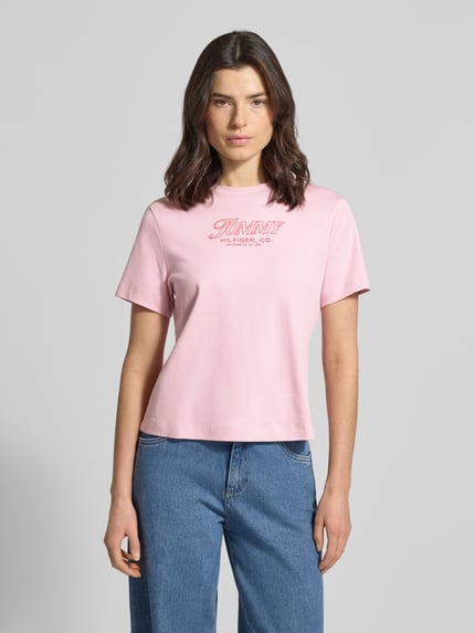 Vrouwenmodel draagt Slim Fit T-Shirt aus reiner Baumwolle van Tommy Hilfiger, roze unikleuren jersey, labelprint, ronde hals, korte mouw, frontale totale weergave.