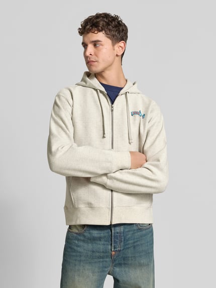 Męski model nosi bluzę rozpinaną z nadrukiem z logo 'Sweatjacke mit Label-Print' od Kenzo z bawełny, luźny krój, kaptur z tunelem, długość tyłu w rozmiarze M: 67 cm, szerokość ramion w rozmiarze M: 55 cm, długość rękawów w rozmiarze M: 64 cm, jasnoszara, gładka faktura, widok całej sylwetki z przodu.