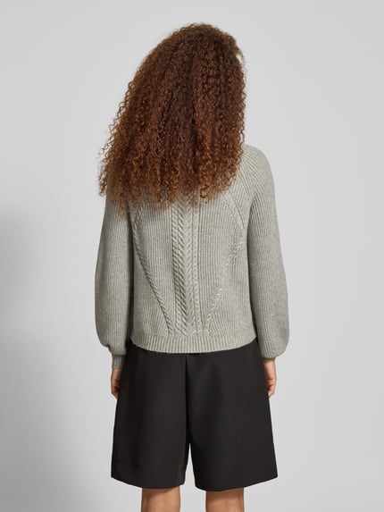Frauenmodel trägt Regular Fit Strickpullover aus Viskose-Mix Modell 'KATIA' von Only in Melange-Optik mit Zopfmuster, Ganzkörperansicht Rückansicht.