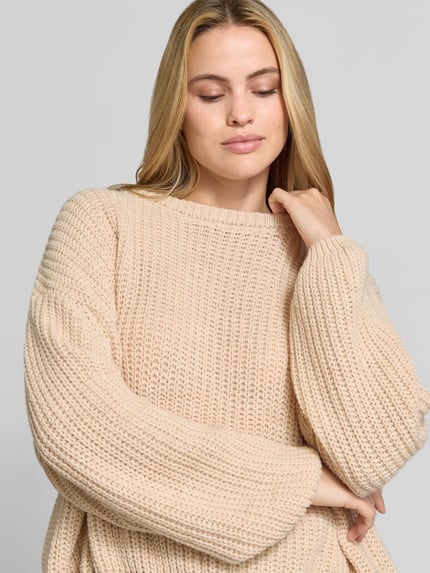 Frauenmodel trägt Oversized Strickpullover aus Leinen-Mix von American Vintage in Beige, grob gestrickt, Rundhalsausschnitt, Nahaufnahme Oberkörper.
