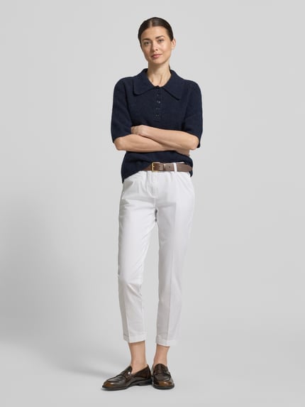Frauenmodel trägt Slim Fit Jeans mit fixierten Beinabschlüssen Modell 'Stella' von Cambio, bawełniany elastyczny materiał, kolor biały, kieszenie z tyłu, kieszonka na monety, zapięcie na guzik i zamek, szerokość w rozmiarze 36: 41 cm, długość wewnętrzna nogawki w rozmiarze 36: 69 cm, krój slim fit, widok całej sylwetki z przodu