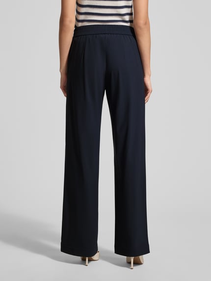 Frauenmodel trägt Hose mit elastischem Bund Modell 'COSMEA' von Raffaello Rossi im Material-Mix mit Stretch-Anteil, weites Bein, Längsnähte, dunkle Farbe, glatte Textur, Ganzkörperansicht Rückansicht.