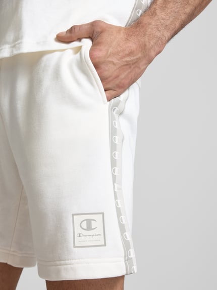 Männermodel trägt Shorts mit Logo und elastischem Bund von CHAMPION in Cremeweiß, Baumwoll-Mix, Regular Fit, Nahaufnahme Oberschenkel.