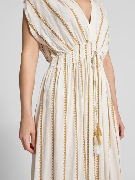 Frauenmodel trägt Maxikleid aus reiner Viskose von ZABAIONE, cremefarben mit goldenen Zickzack-Streifen, Nahaufnahme Oberkörper. Taillierte Passform, elastische Taille mit Zierbändern, V-Ausschnitt, kurzärmliges Design, moderne Textur, Kontext: Damen Maxikleid von ZABAIONE, Rückenlänge 131 cm, Brustweite 41 cm.