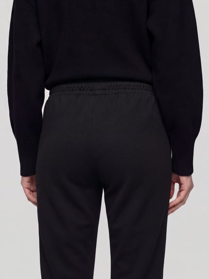 Frauenmodel trägt Regular Fit Pyjama-Hose mit Kontraststreifen von BOSS, mehrfarbig gestreift, Jersey, High Waist, seitliche Eingrifftaschen, Ganzkörperansicht Rückansicht.