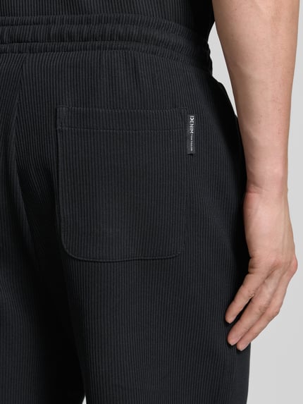 Männermodel trägt Relaxed Fit Sweatshorts aus reiner Baumwolle von Tom Tailor Denim in Optik: Unifarben, Gesäßtasche, Rippstrick-Optik, Nahaufnahme Gesäßtasche.