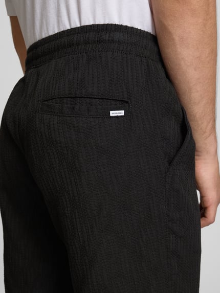 Mężczyznamodel nosi Shorts mit Strukturmuster Modell 'JAIDEN' von Jack & Jones, czarny kolor, materiał z bawełną, krój regular fit, strukturalna faktura, szerokość w rozmiarze M: 41 cm, długość wewnętrzna nogawki: 21 cm, zbliżenie na tył