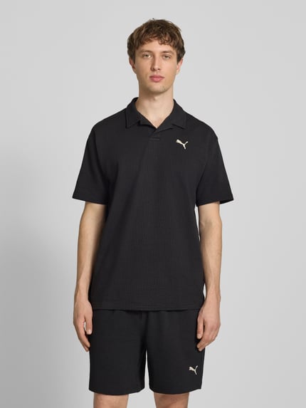 Mężczyznamodel nosi Regular Fit T-Shirt mit Logo-Stitching von PUMA PERFORMANCE, czarny bawełniany miks ze strukturą, krój regular fit, z kołnierzykiem rewers, logo na piersi, długość tyłu w rozmiarze M: 74 cm, całkowity widok z przodu.