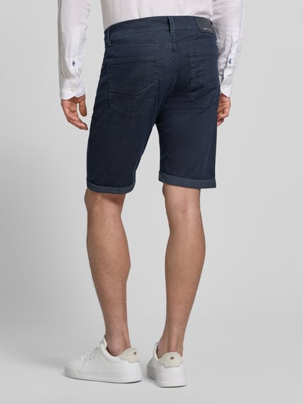 Männermodel trägt Jeansshorts mit Label-Detail von Pierre Cardin in Dunkelblau, Baumwoll-Mix mit Stretch-Anteil, Ganzkörperansicht Rückansicht. Regular-Fit, Eingrifftaschen, Umschlag, Bundweite bei Größe 32: 42 cm, Innenbeinlänge bei Größe 32: 26 cm.