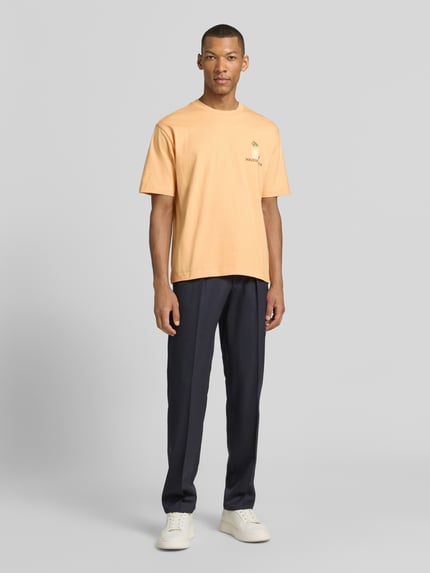 Männermodel trägt T-Shirt mit rückseitigem Motiv-Print von MCNEAL in Orange, Bio-Baumwolle, gerader Schnitt, Ganzkörperansicht von vorne.