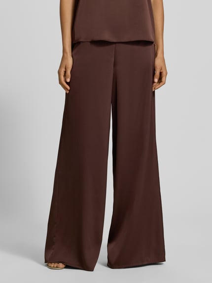 Frauenmodel trägt Wide Fit Stoffhose aus Satin von VM by Vera Mont in Dunkelbraun, glatte Textur, teilelastischer Bund, Nahaufnahme Oberkörper. Damen Stoffhose, Satin, Wide Fit, Bundfalten, Bundweite 38 cm, Innenbeinlänge 83 cm bei Größe 36.