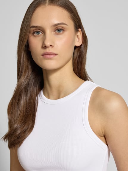 Frauenmodel trägt Tanktop in Ripp-Optik von REVIEW aus Baumwoll-Elasthan-Mix, eng anliegende Passform, Rundhalsausschnitt, Nahaufnahme Oberkörper.