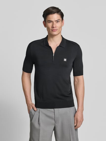 Męski model nosi czarną koszulkę polo Regular Fit Poloshirt aus Viskose-Mix Modell 'SAYFONG-4' von HUGO, efekt: jednolity kolor, aplikacja: naszywka z logo, krój: krój regular fit, kołnierzyk polo, krótka listwa guzikowa, rękaw: krótki rękaw, zakończenie: prążkowane, wykończenie materiału: dżersej, materiał: mieszanka wiskozy. Ganzkörperansicht von vorne.